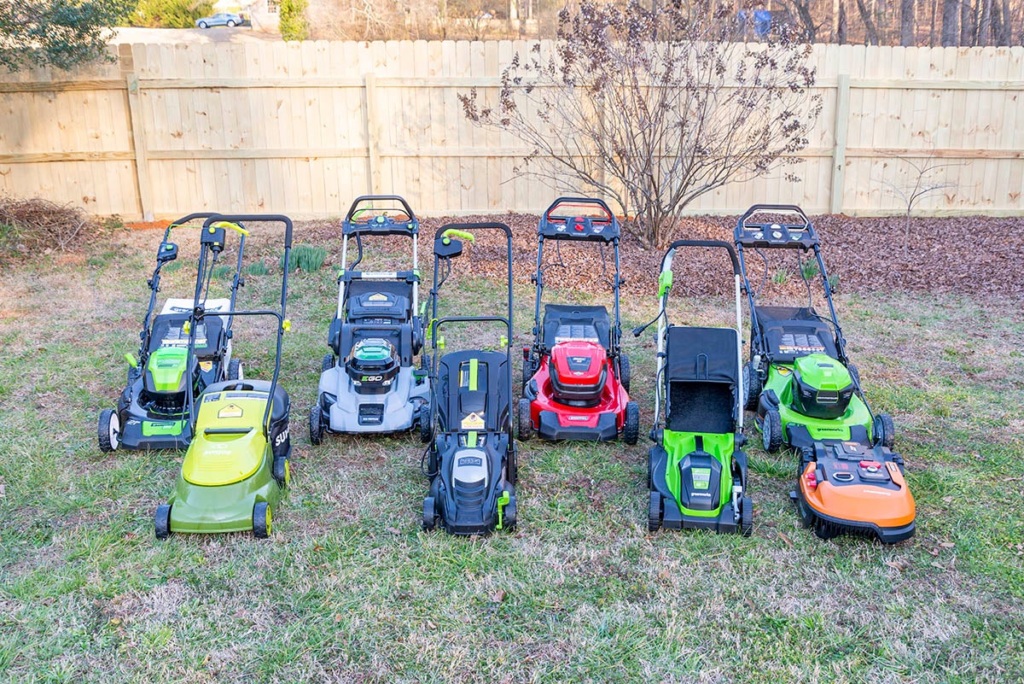 Eight different models of electric lawn mowers sitting on a green lawn.
